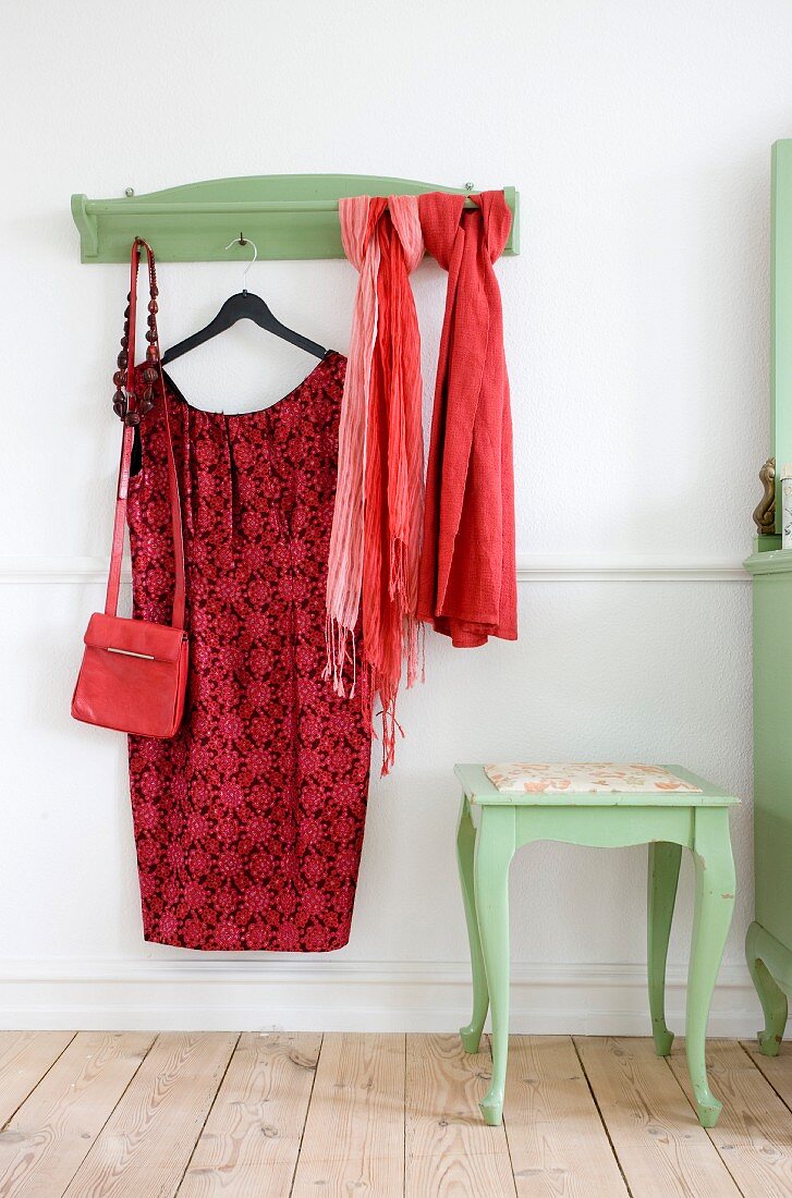 Red dress on coat hanger and scarves hung from green-painted coat rack with matching side table with curved legs