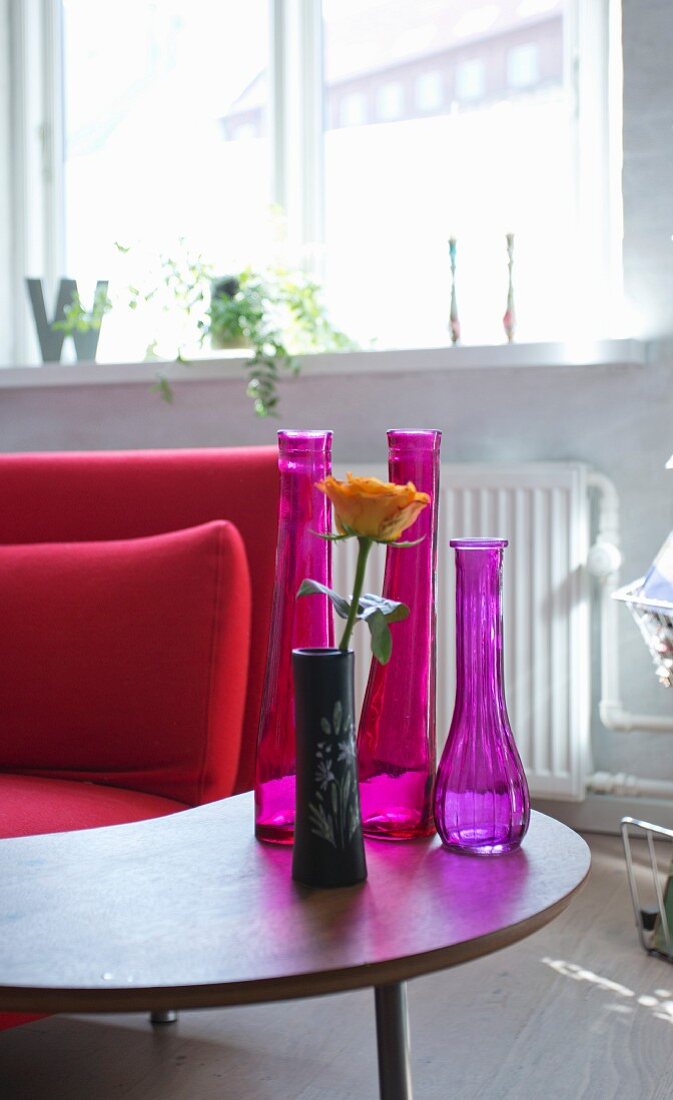 Arrangement of various vases on small retro table next to red sofa in living area