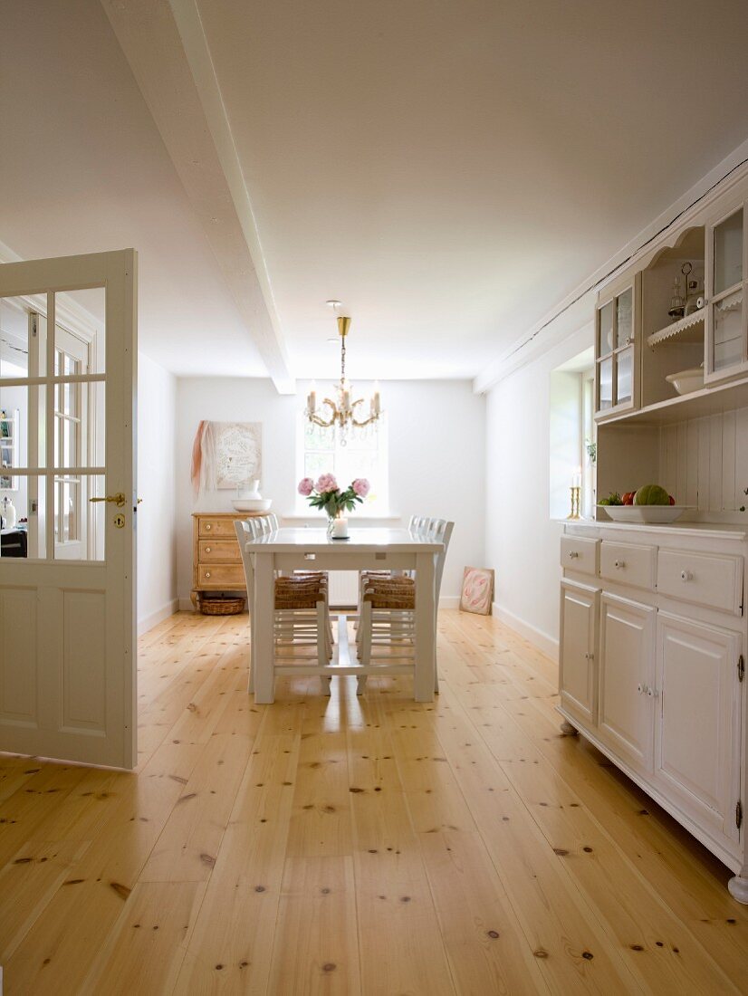 Dining room with white-painted chairs and table and rustic dresser on well-tended wooden floor