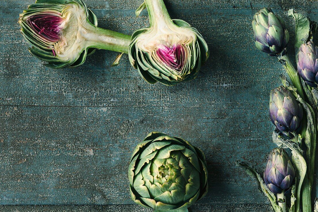 Fresh artichokes, whole and halved, on a wooden surface
