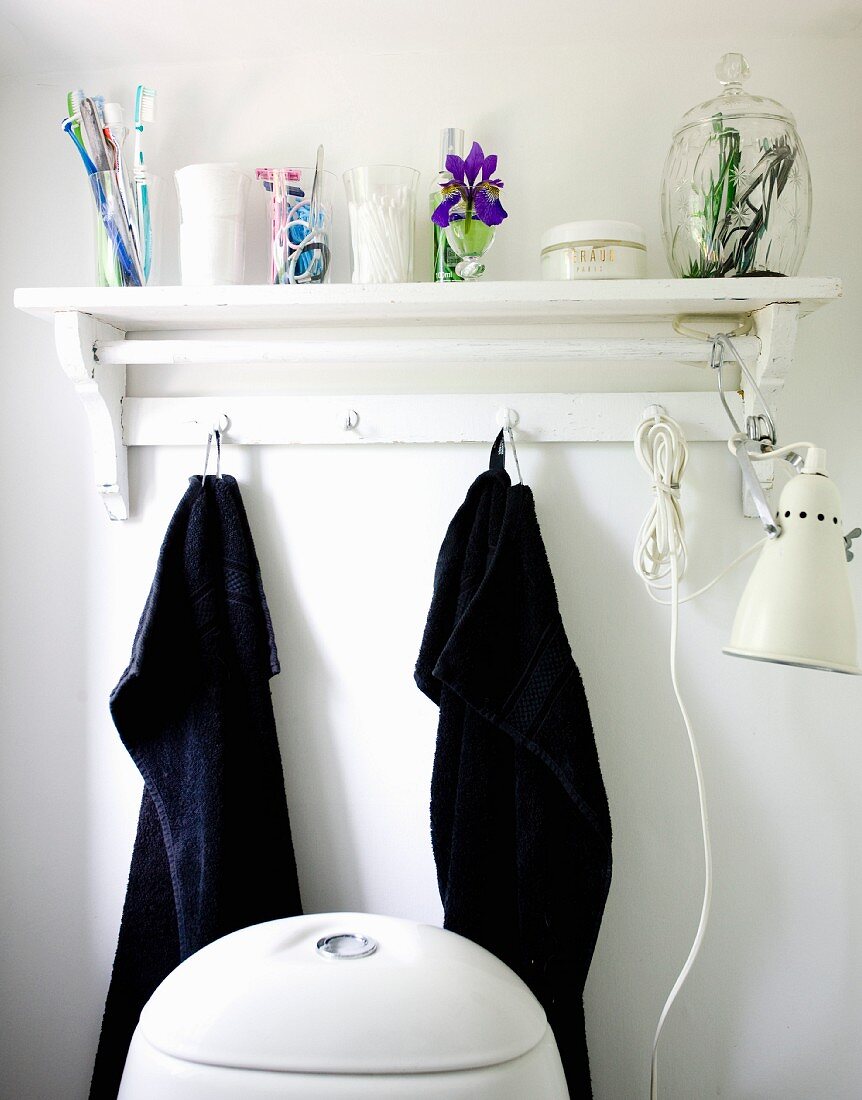 Bathroom utensils on white wall bracket and black towels hung from hooks
