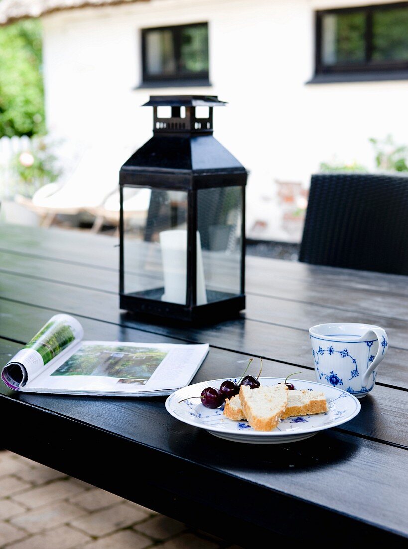 Schwarzer Holztisch mit Geschirr, Zeitschrift und Laterne auf der Terrasse