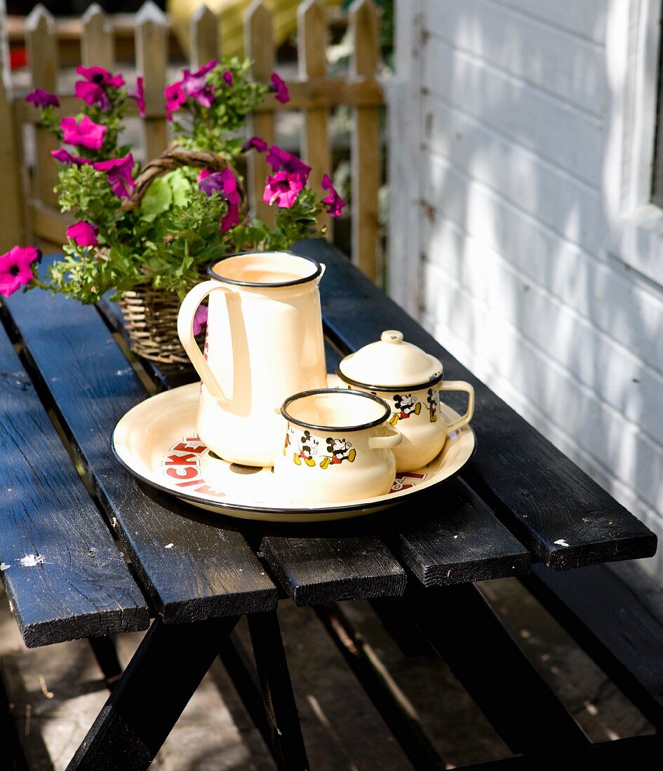 White enamel pots on tray in front of petunia on black garden table