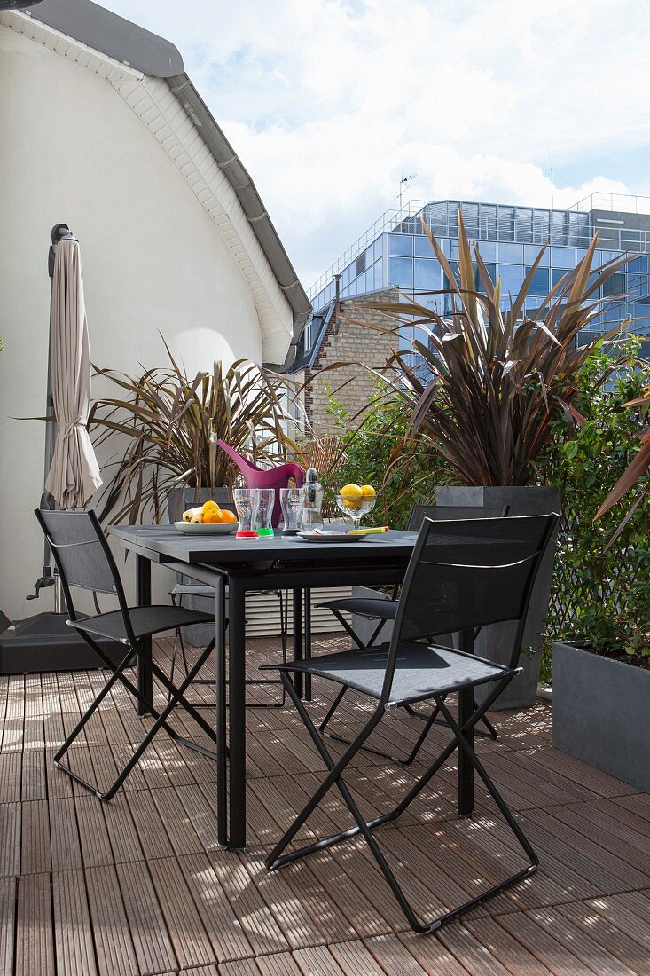 Seating area with modern, black metal furniture, wooden deck and planters on urban roof terrace