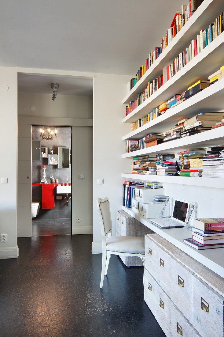 Home office integrated into living space with bookcase and white filing cabinets; view into bathroom in background