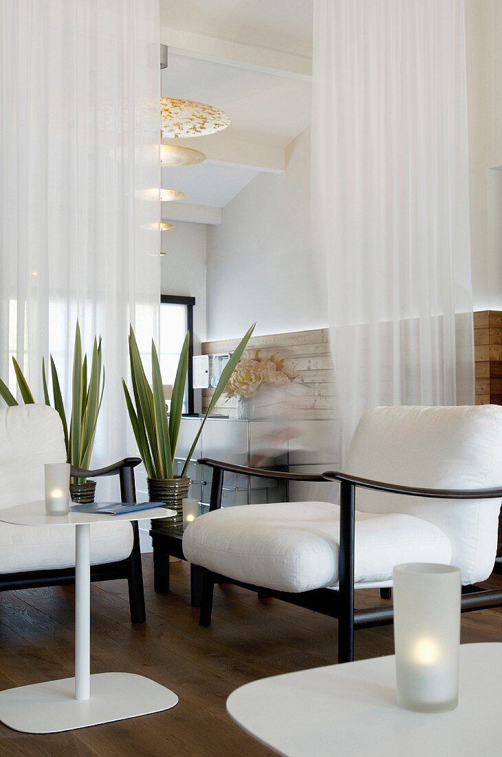 White cushions on black armchair frames and purist side table in front of delicate curtain used as partition