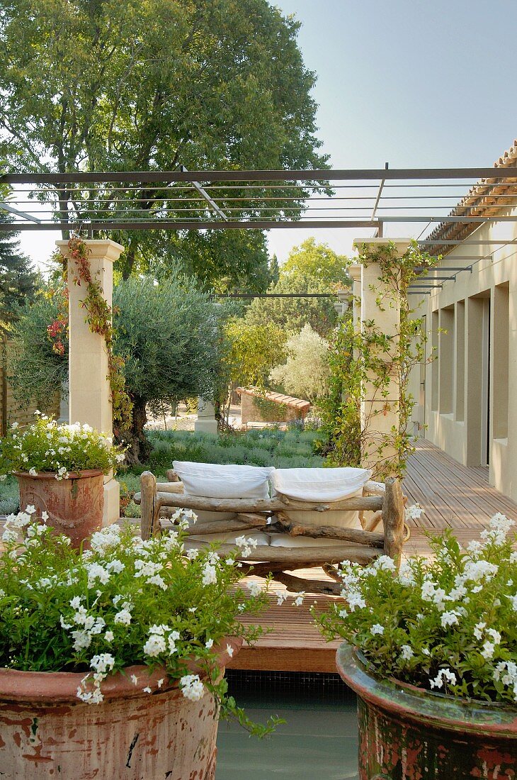 Mediterranean wooden deck with potted plants and rustic tree-trunk sofa