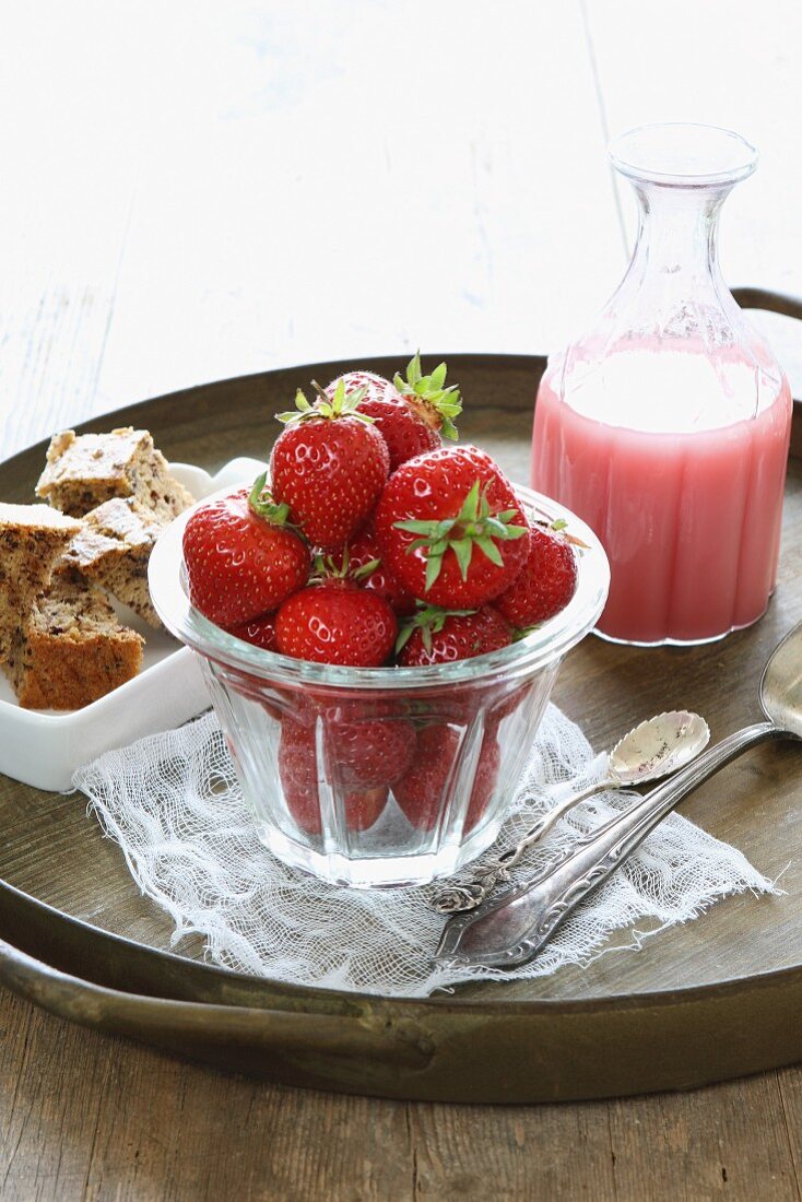 Frische Erdbeeren im Glas und selbstgemachte Erdbeermilch, dahinter Schälchen mit Topfkuchenstücken