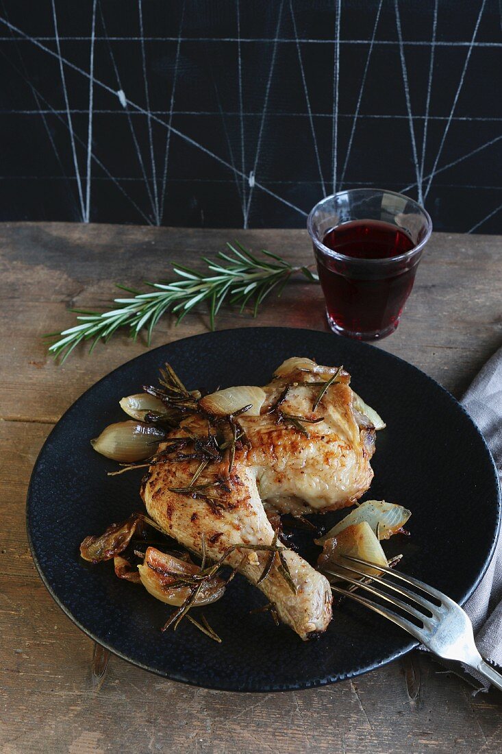 A chicken leg with onions and rosemary served with a glass of red wine