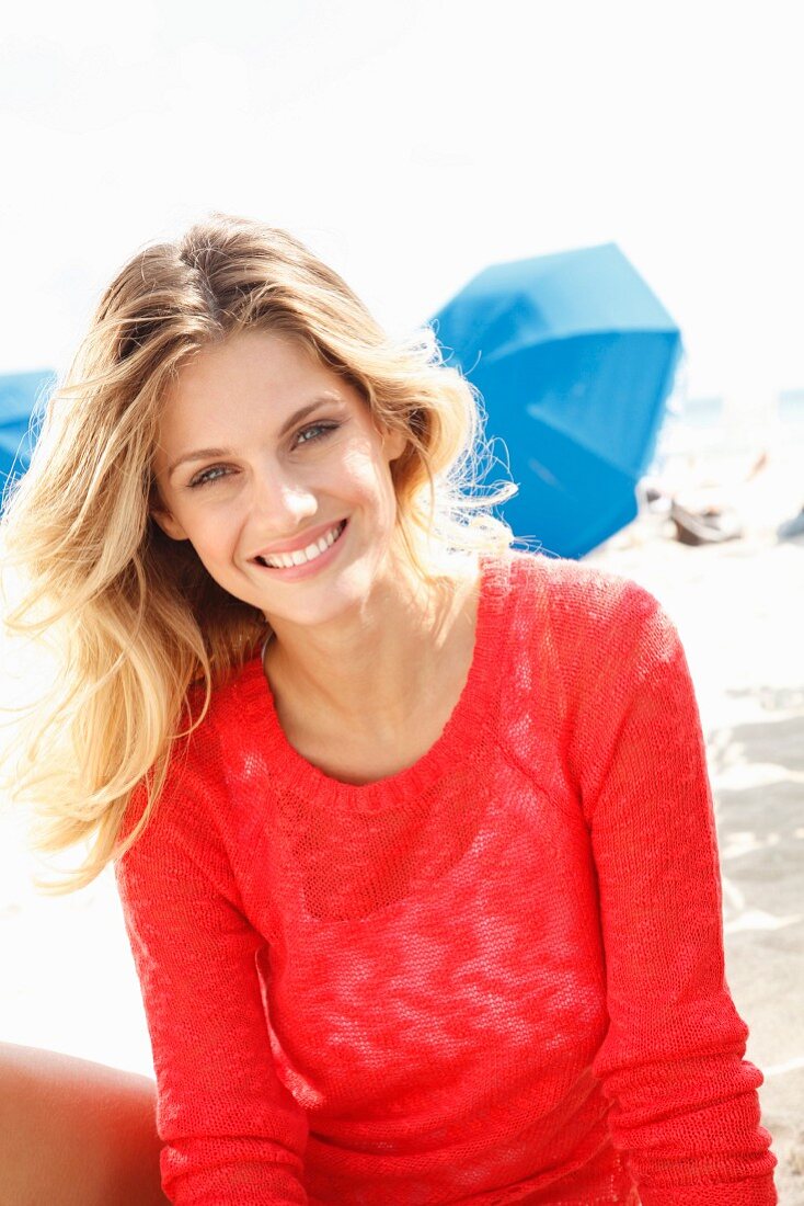 A young blonde woman on a beach wearing a transparent red knitted jumper