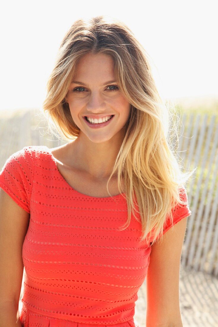 Junge blonde Frau in lachsfarbenem Shirt am Strand