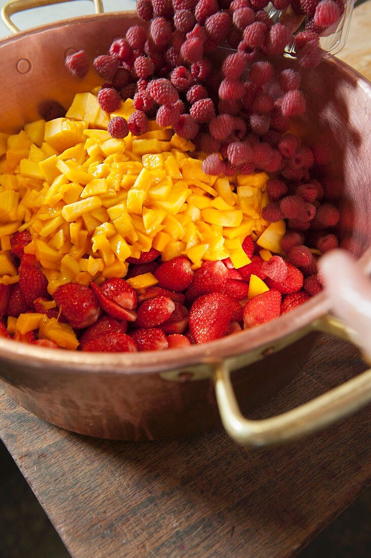 Mangos, raspberries and strawberries being placed in a copper pot for making jam