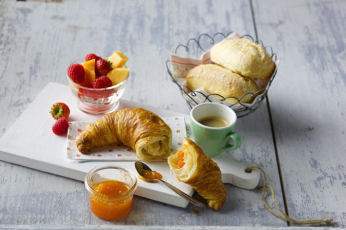 Frühstück mit Croissant, Marmelade, Espresso, Brötchen und Obst