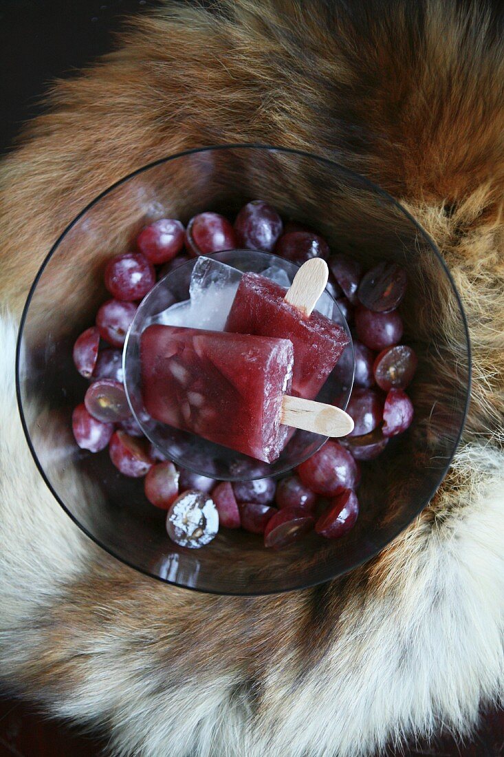 Rotes Traubeneis am Stiel in Glasschale auf Tierfell