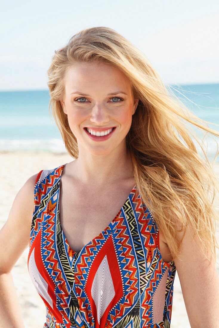 A young blonde woman on a beach wearing an ethnic patterned summer dress