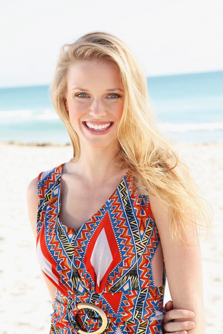 A young blonde woman on a beach wearing an ethnic patterned summer dress