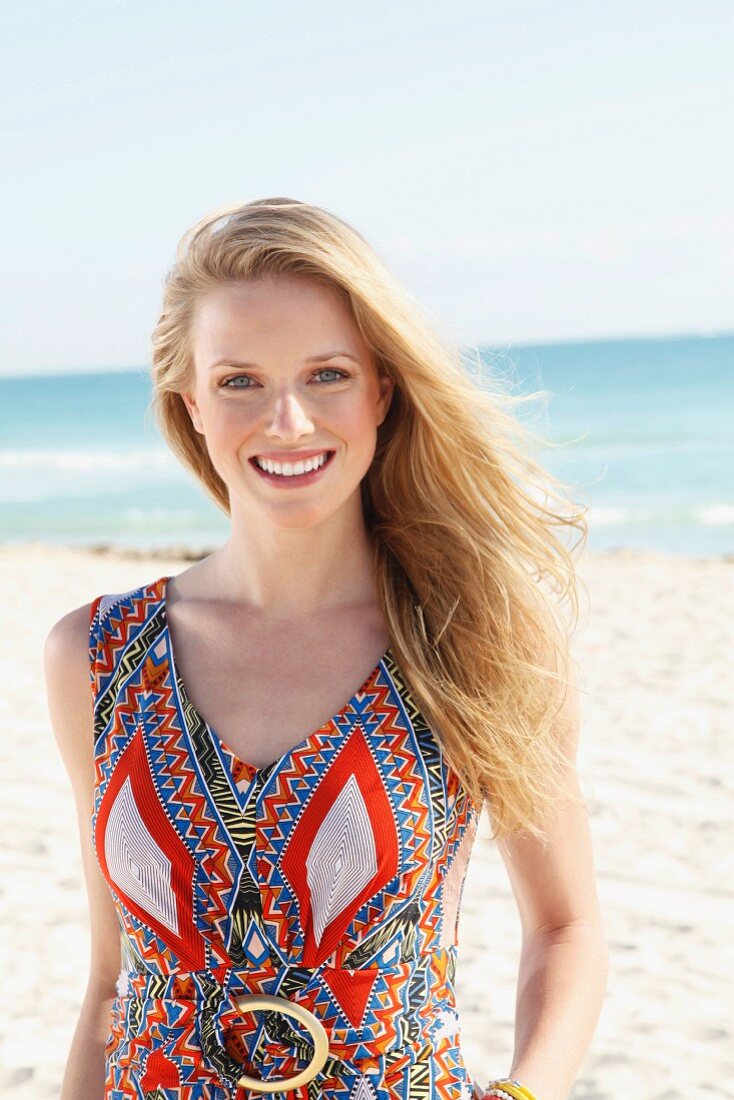 A young blonde woman on a beach wearing an ethnic patterned summer dress