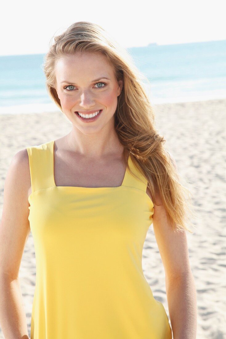 A young blonde woman on a beach wearing a yellow summer dress