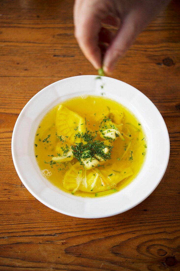 Fish soup with sage ravioli being sprinkled with herbs
