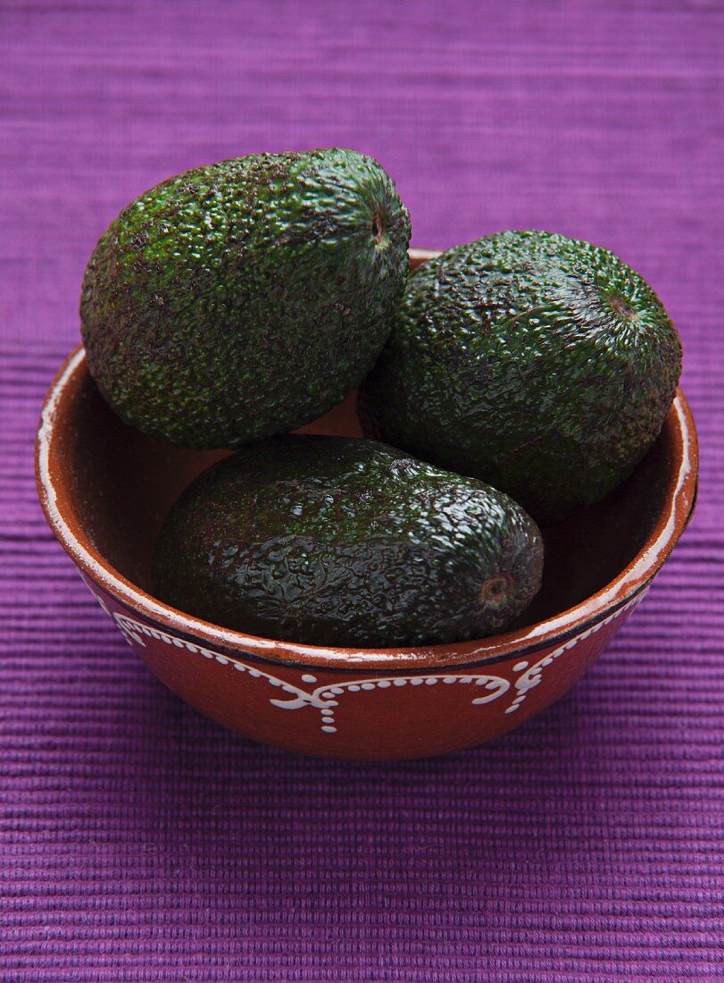 Three avocados in a ceramic bowl