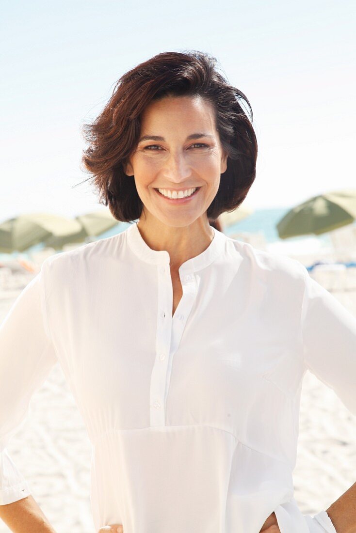 A brunette woman on a beach wearing a thin white blouse