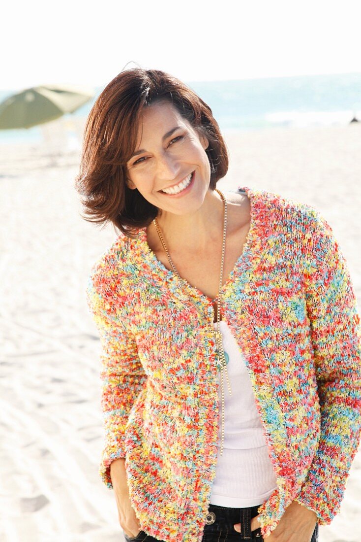 Brünette Frau in weißem Shirt und bunter Strickjacke am Strand