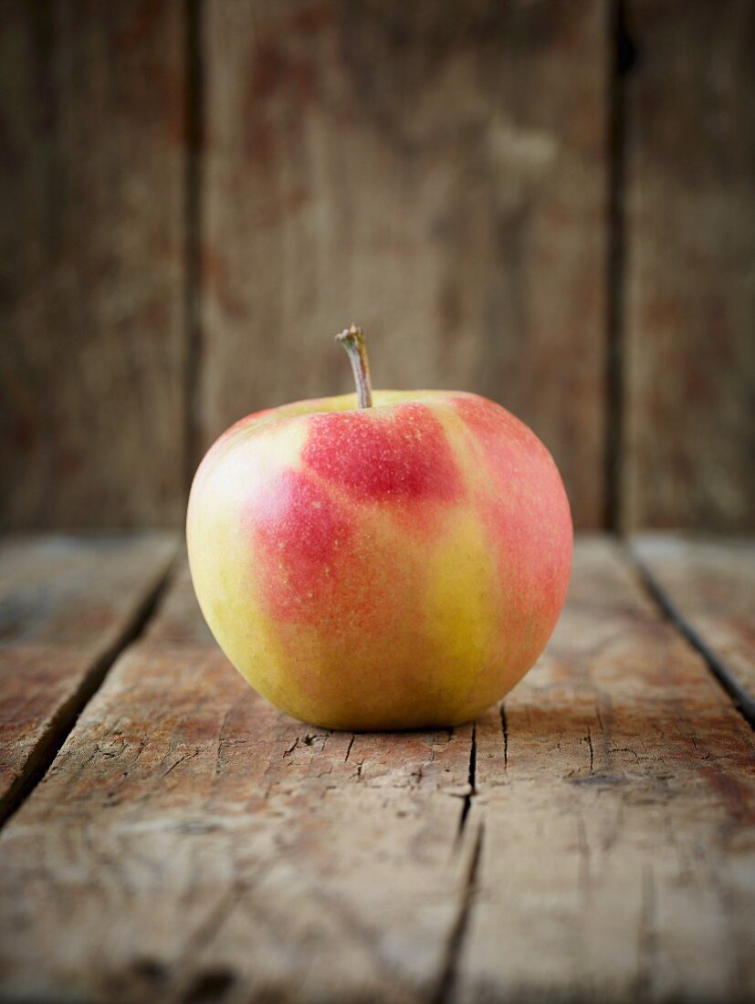 A red and yellow apple on an old, brown wooden surface in front of a wooden wall