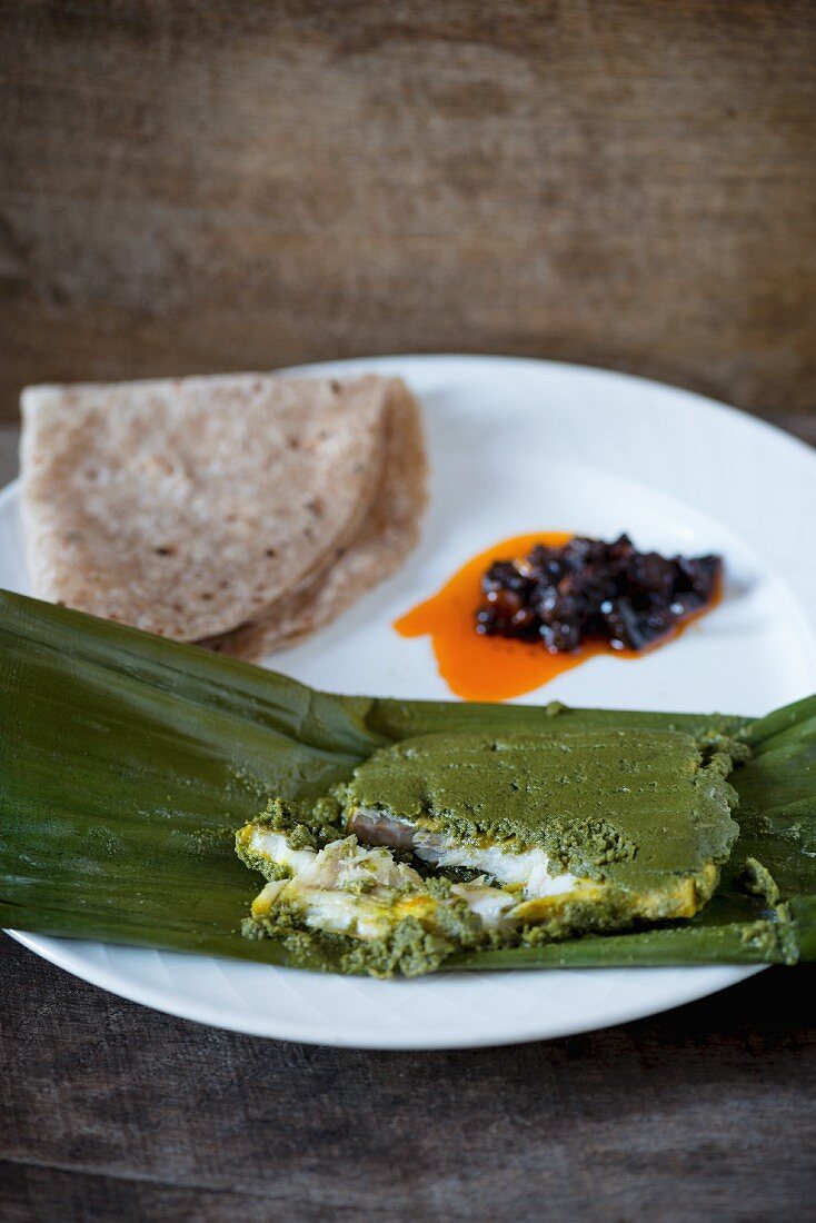 Fish in a herb and chilli marinade wrapped in a banana leaf with chapati and pickles
