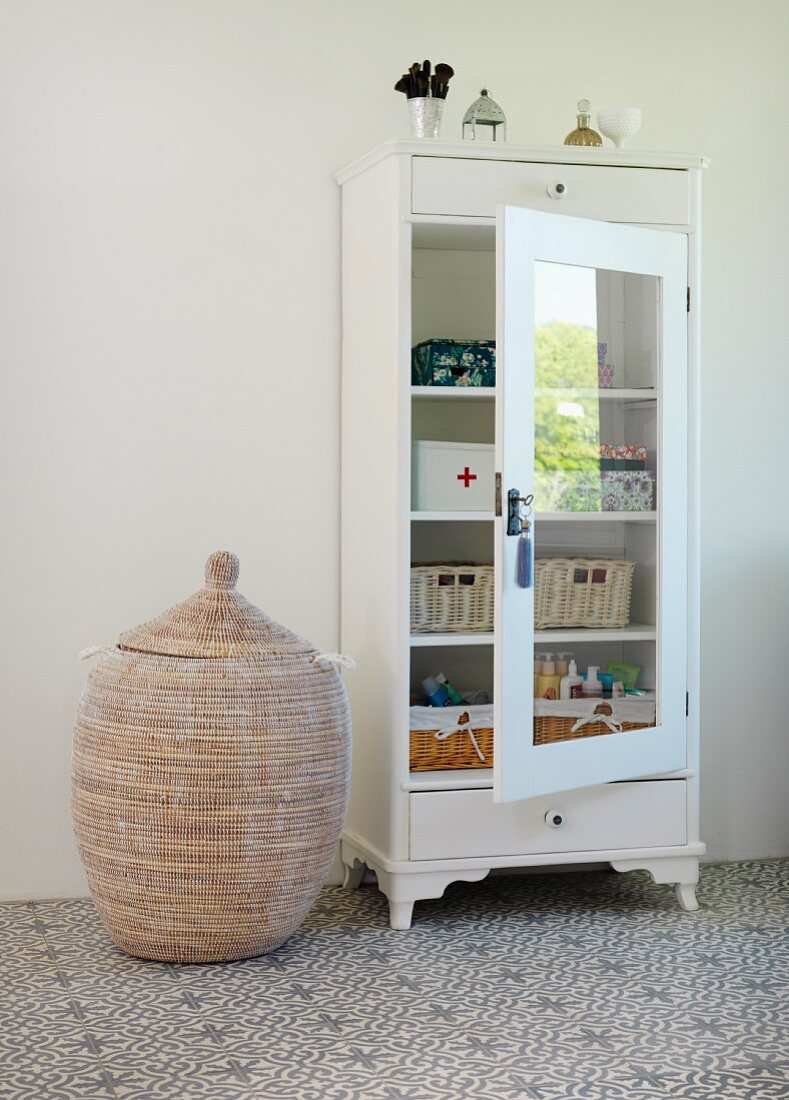 Baskets in white-painted, glass-fronted cupboard on cement-tiled floor