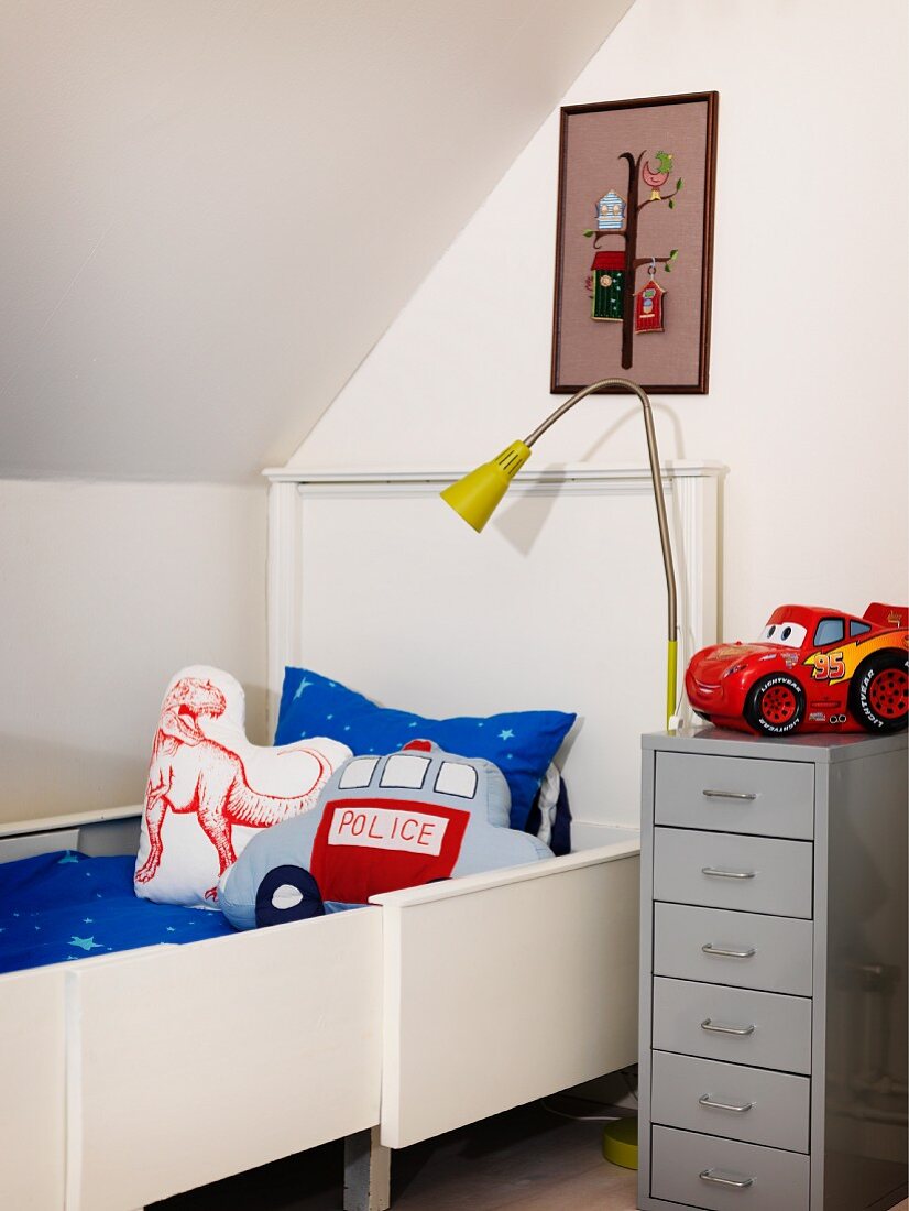 Boy's bedroom with white, extendible bed, scatter cushions, grey filing cabinet and standard lamp