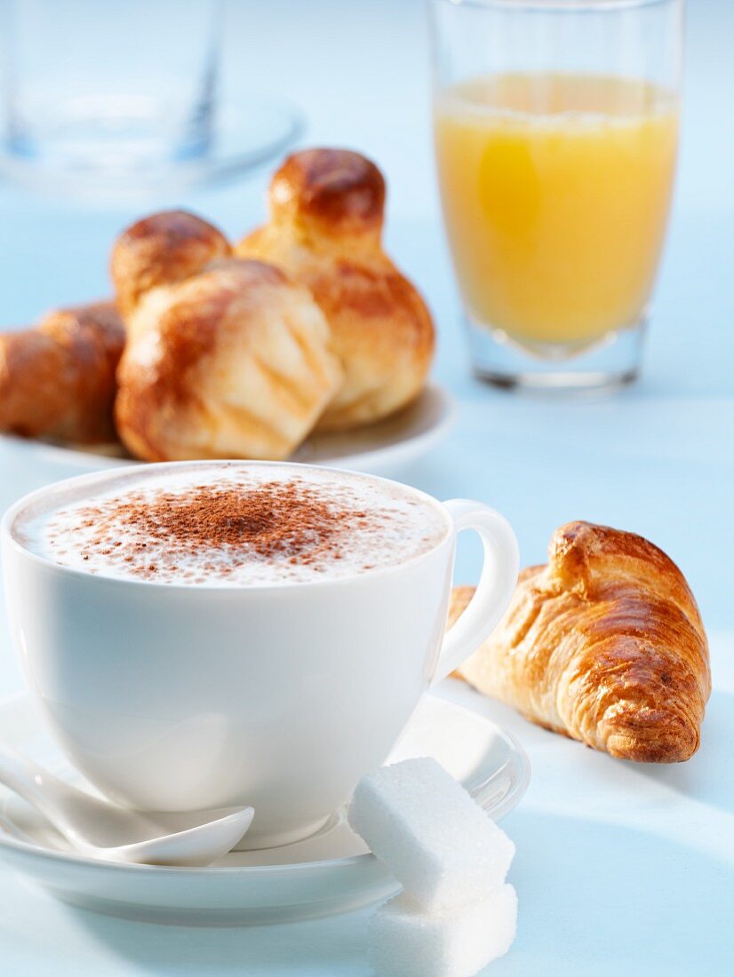 A cappuccino, a croissant, brioche and a glass of orange juice