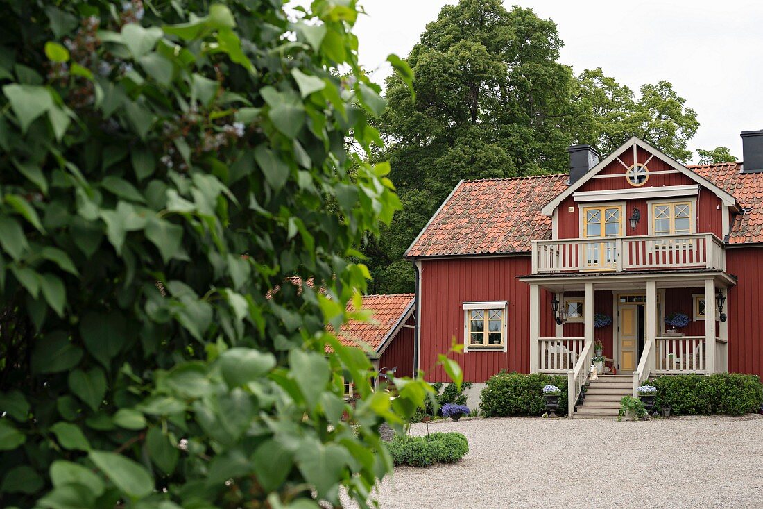 Blick von Garten auf rotbraunes Landhaus, Balkon über Veranda mit Aussentreppe weiss gestrichen