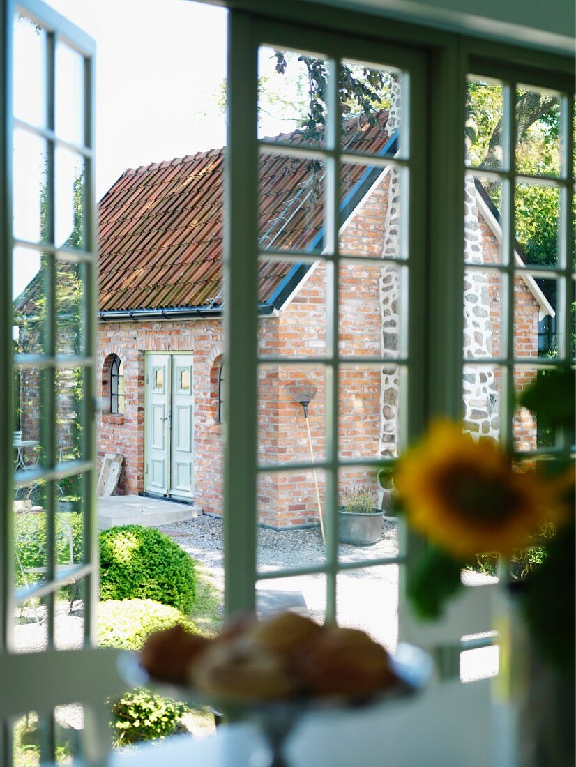 Blick durch offene Terrassentür in den Garten, im Hintergrund kleines Ziegelhaus