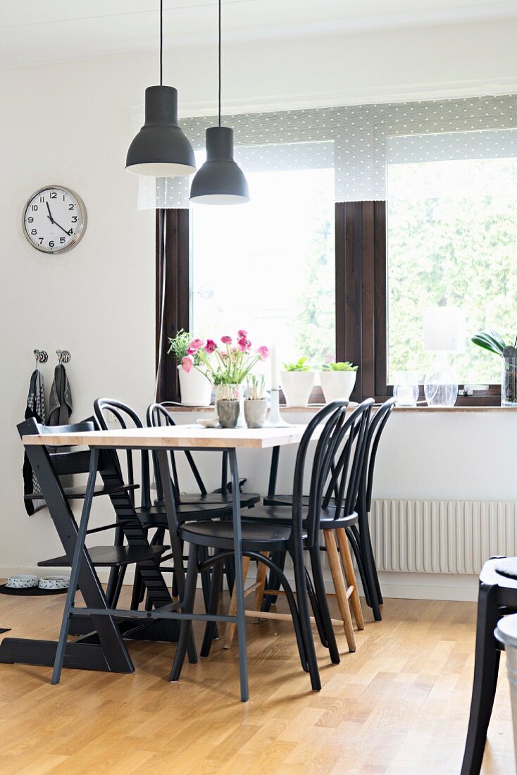 Black Thonet chairs around dining table below pendant lamps with black lampshades next to window