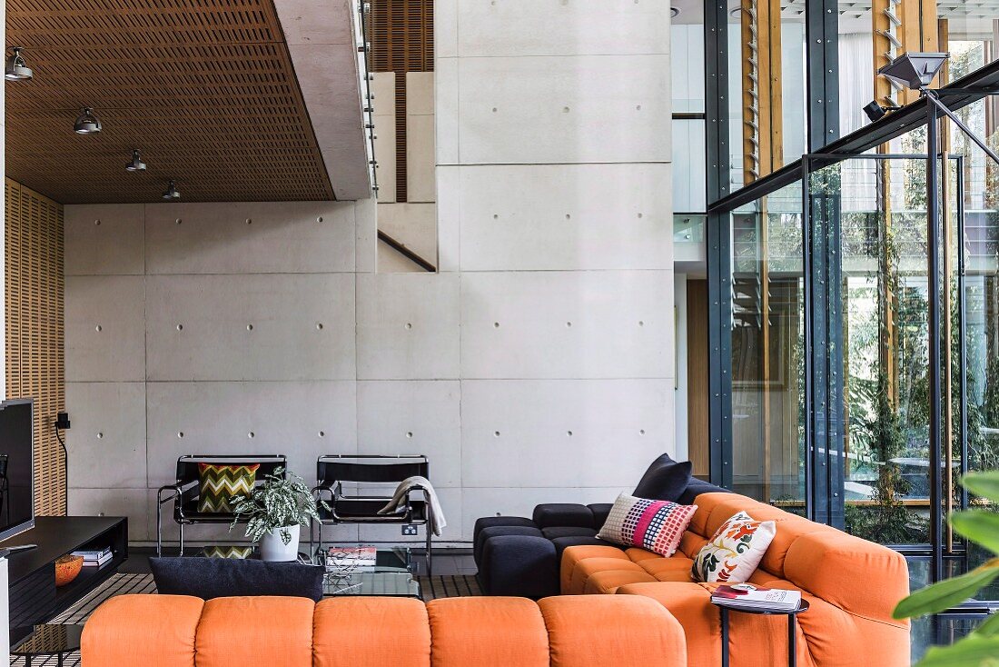 Moderne Lounge mit orangefarbenem Polstersofa unter Galerie, im Hintergrund Sichtbetonwand in zeitgenössischer Architektur