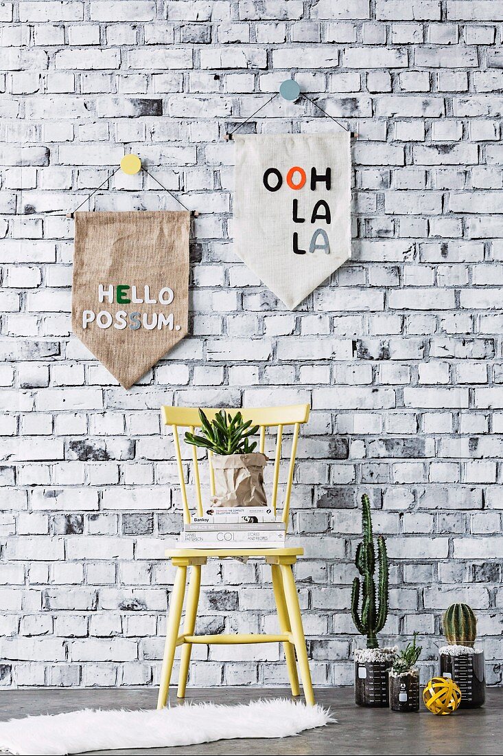 Homemade pennants in front of wallpaper with a brick wall motif, in front of a wooden chair and cacti