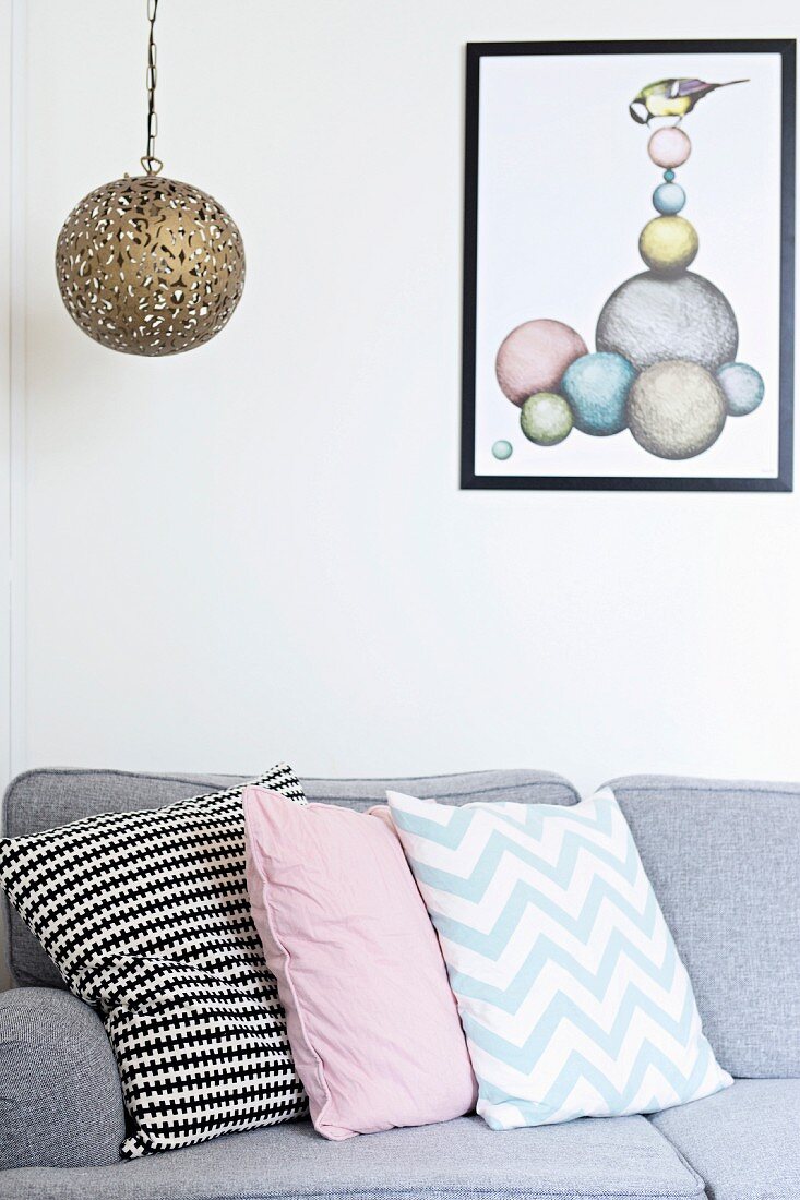 Patterned scatter cushions arranged on grey sofa below pendant lamp with spherical metal lampshade