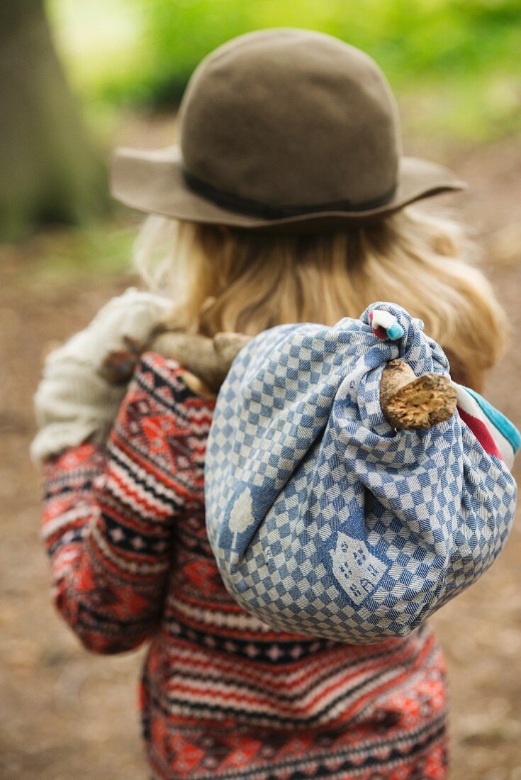 Blonde girl carrying picnic in bindle in autumnal garden