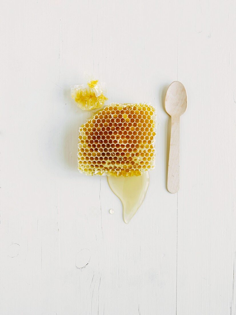 Eine Honigwabe mit Honig auf weißem Holzuntergrund (Aufsicht)