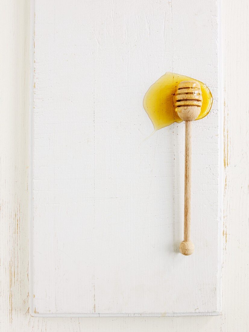 Honey on a honey spoon on a white wooden surface (seen from above)