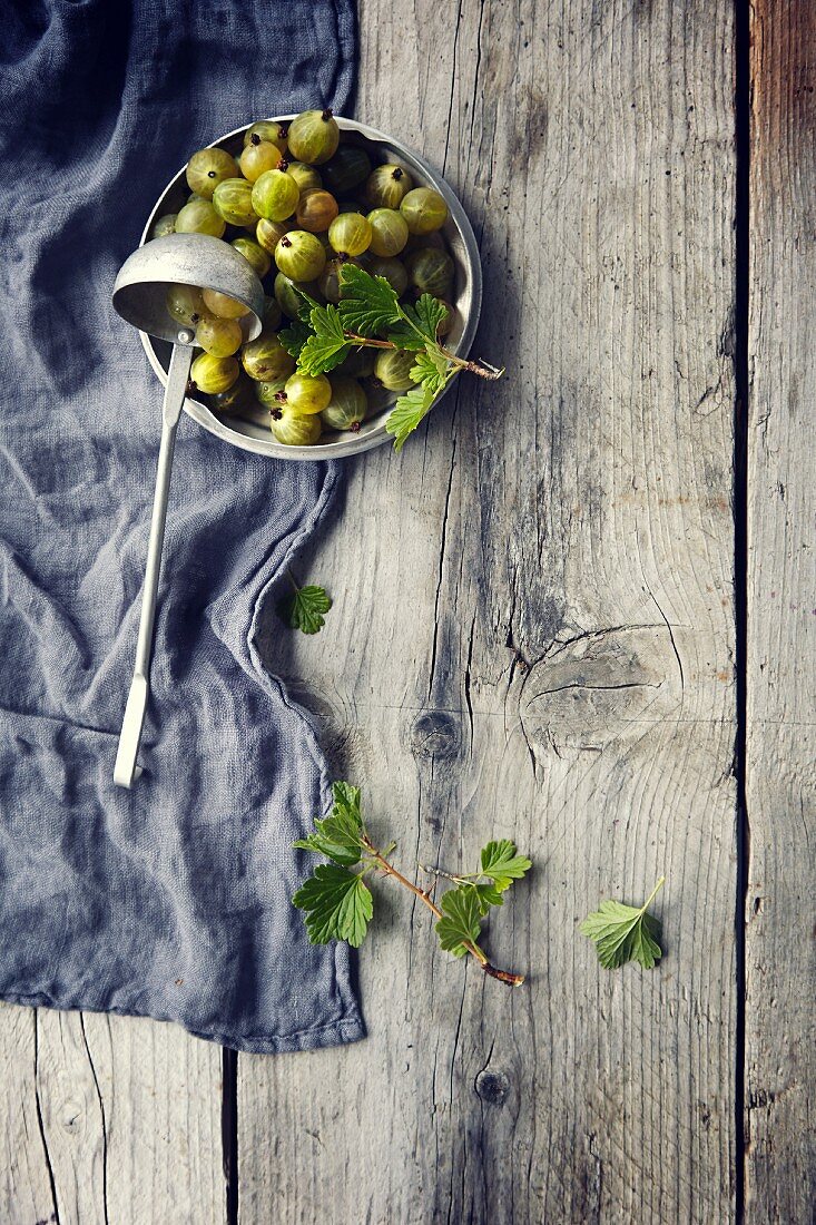 Green gooseberries with leaves in a bowl with a ladle