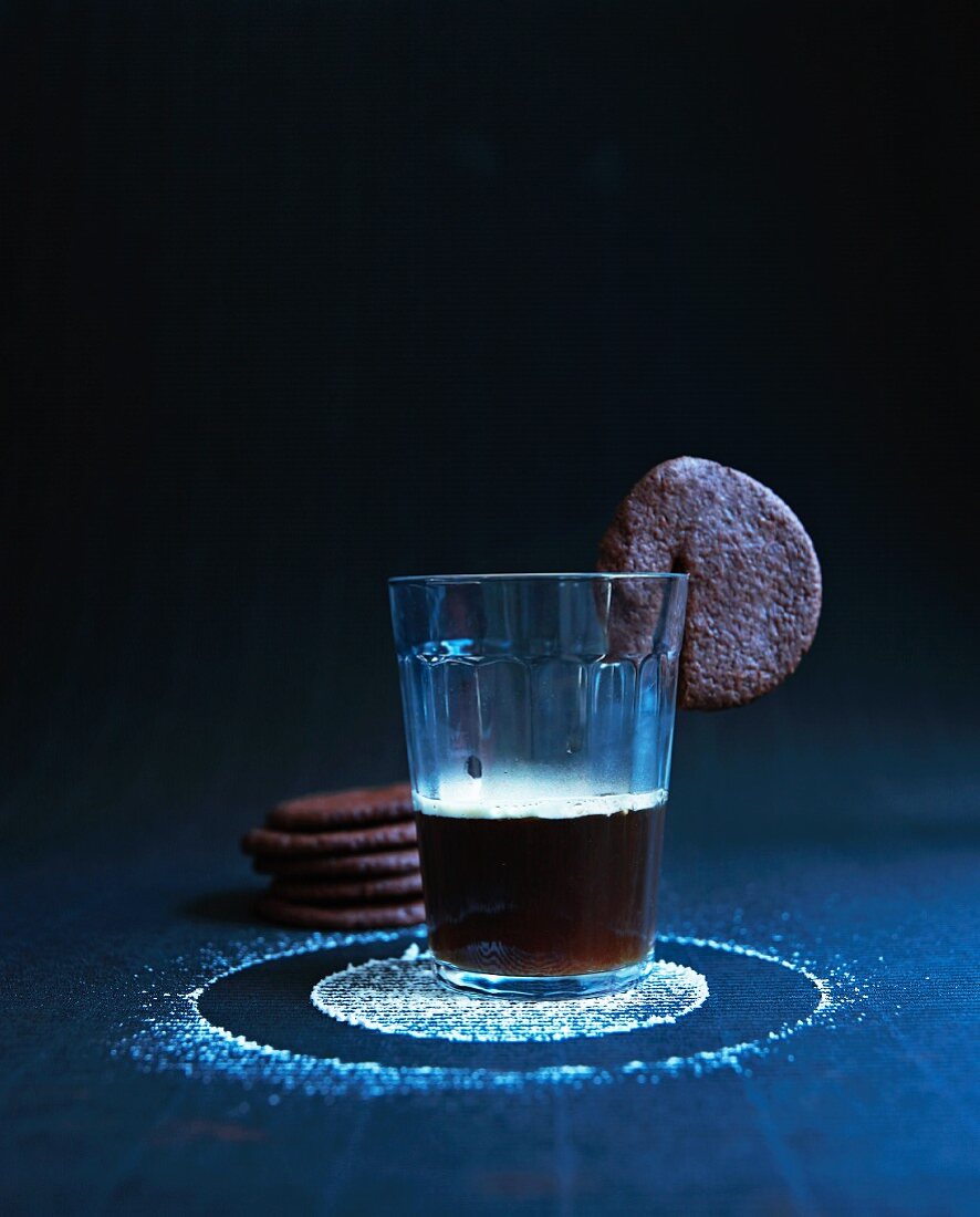A glass of coffee with a chocolate biscuit on the rim