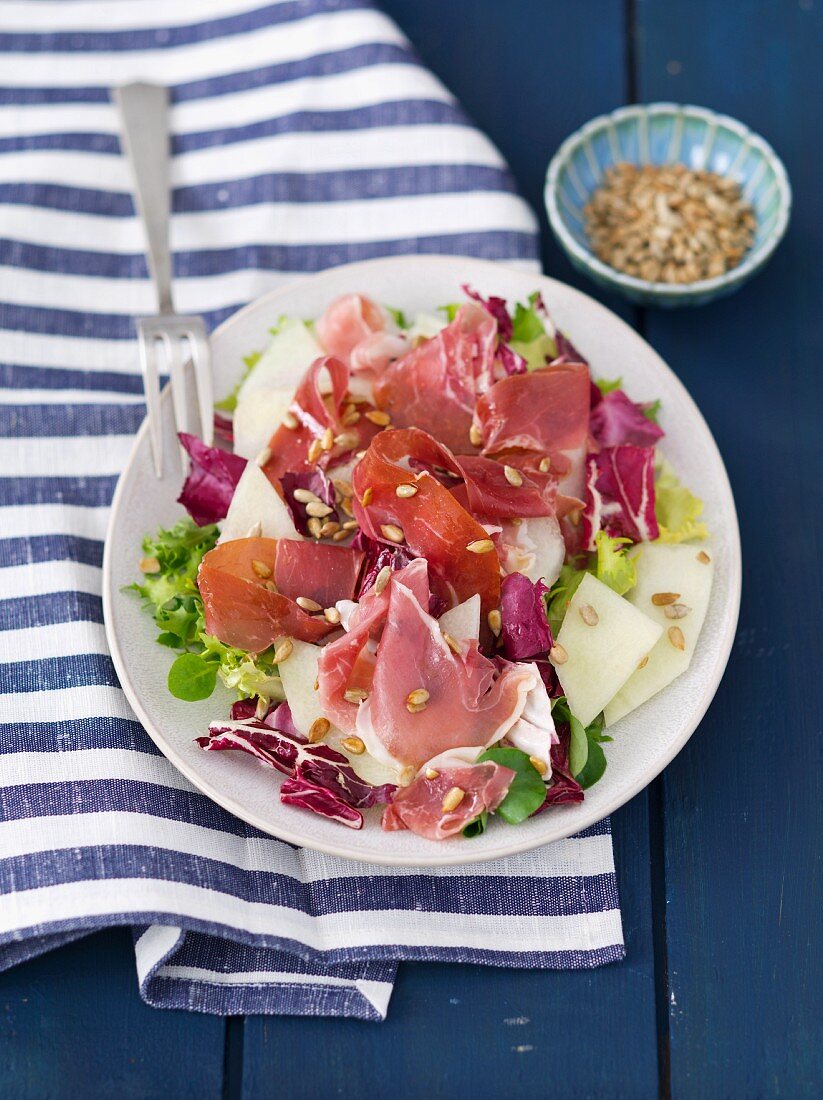 A mixed lettuce with melon, ham and sunflower seeds