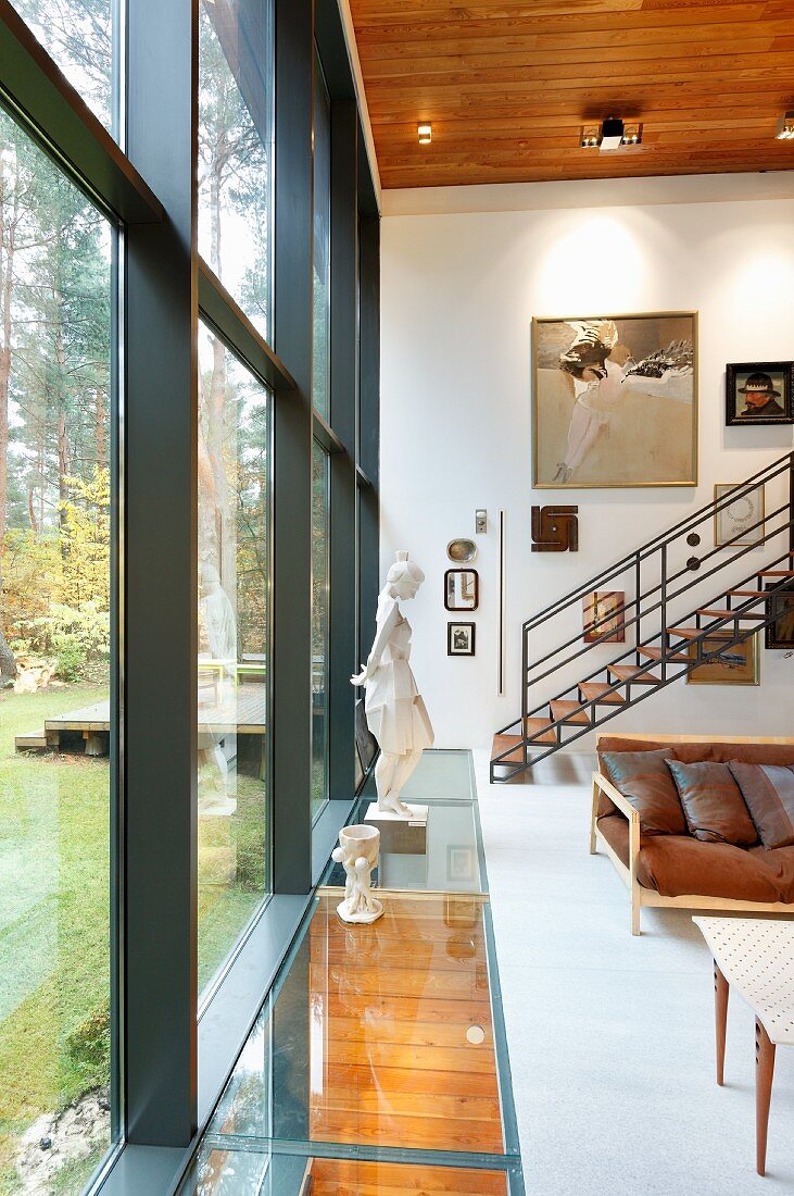 Living room with double-height glass wall and sculpture on glazed strip of floor