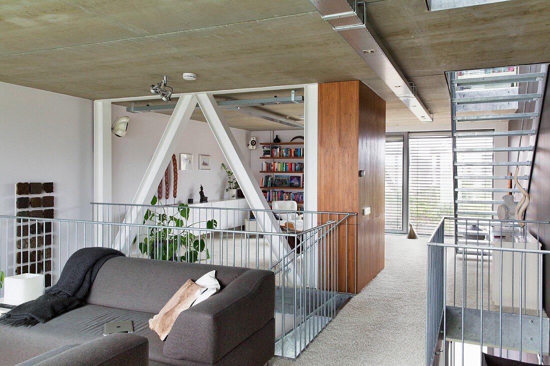 Graues Sofa vor Treppengeländer aus Edelstahl, im Hintergrund Loungebereich in offenem Wohnraum zeitgenössischer Architektur