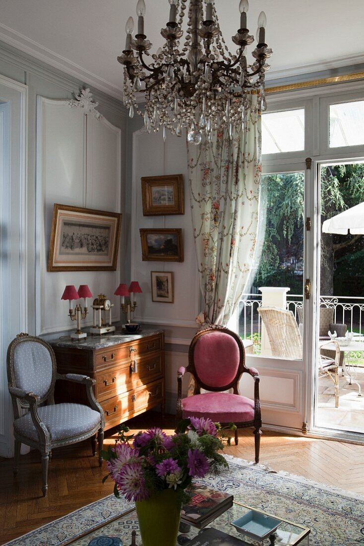 Rococo-style chairs next to chest of drawers in corner below crystal chandelier