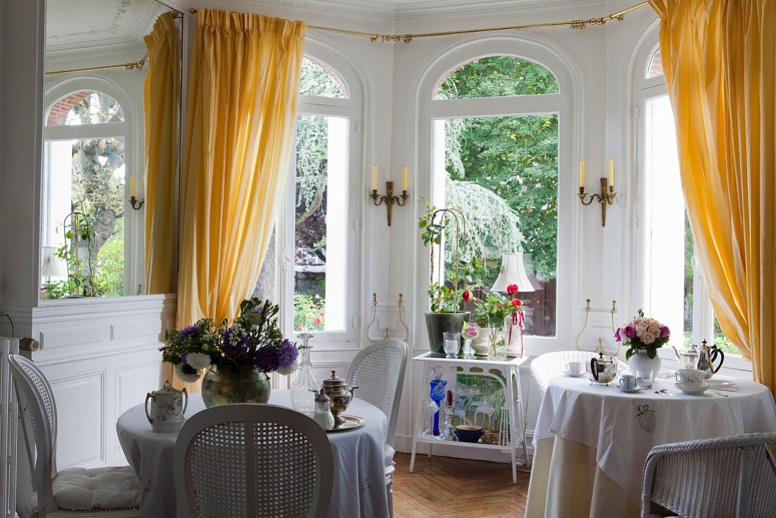 Set bistro tables in front of arched windows with yellow curtains in grand window bay