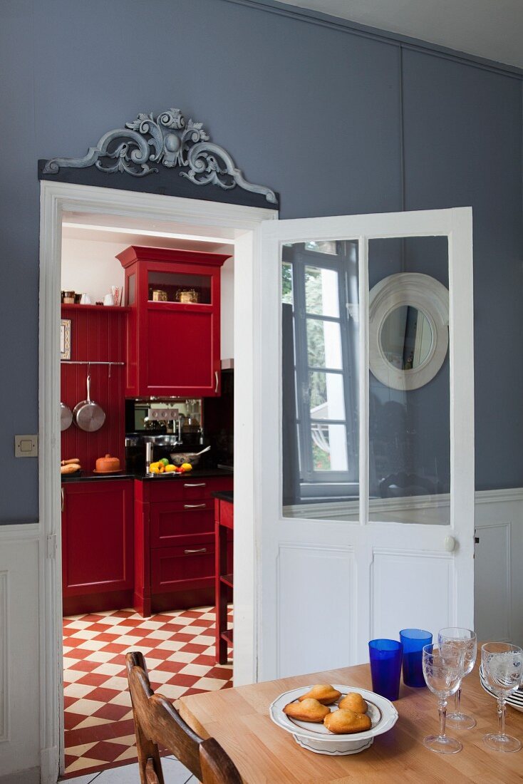 Esstisch vor offener Tür und Blick auf rot lackierte Schränke in der Küche