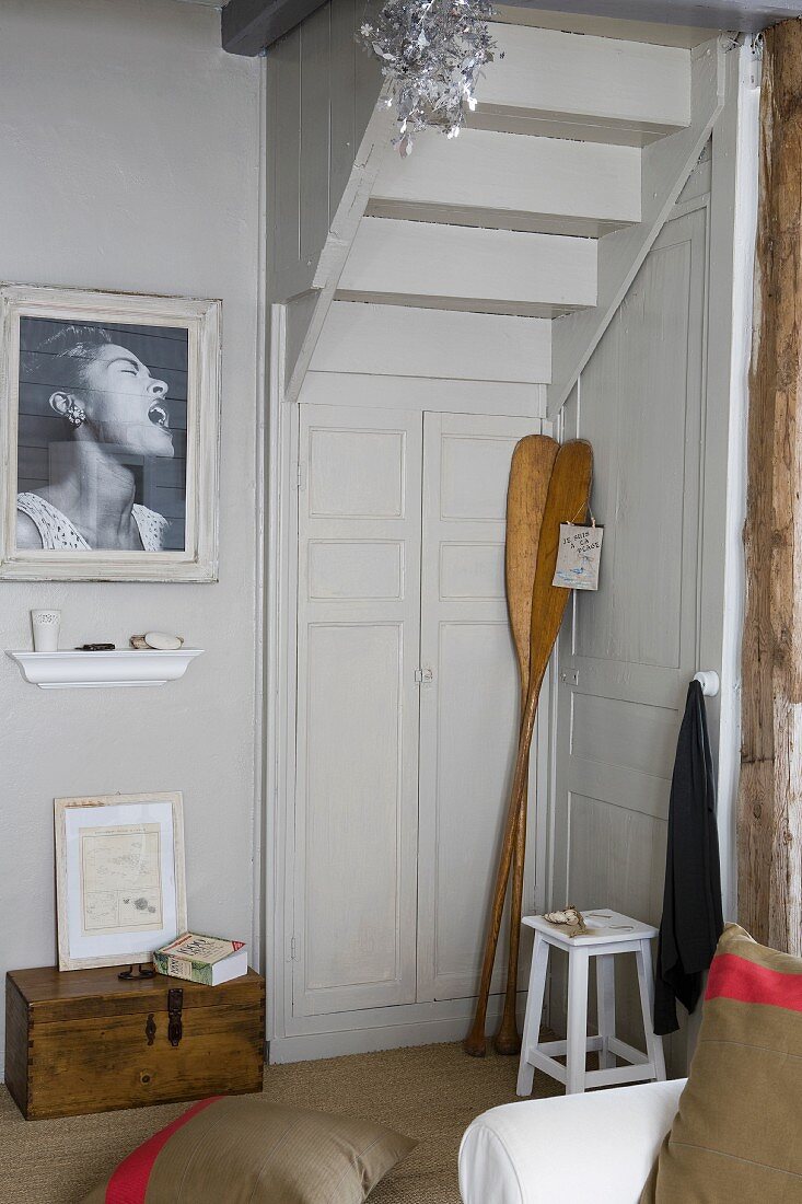 Antike Holzpaddeln in Zimmerecke unter Treppenlauf, seitlich schwarz-weisses Foto an Wand