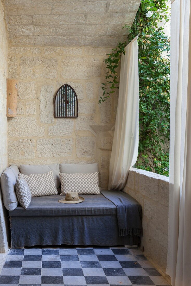 Gemütliche Sitzbank mit grauer Husse und Kissen auf Balkon mit Natursteinwänden